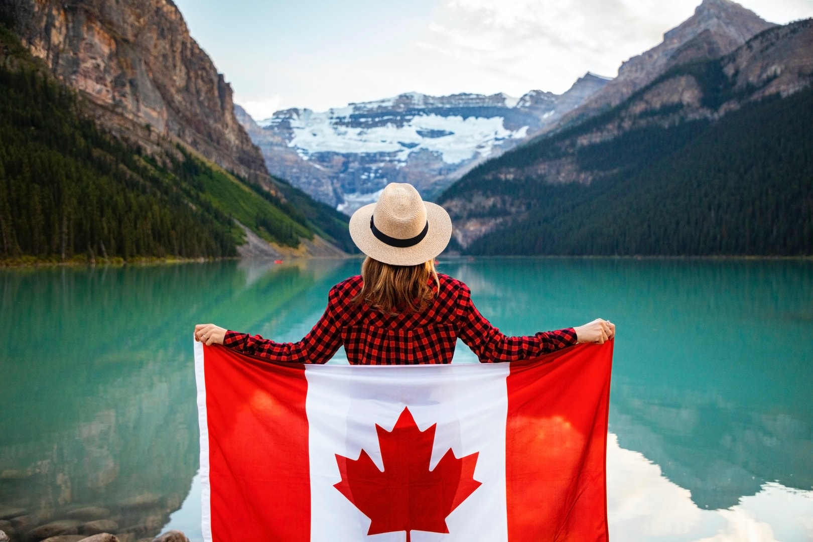 Personne tenant le drapeau canadien devant un lac alpin
